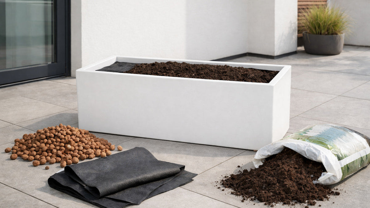 Weißer Pflanztrog beim Bepflanzen mit Blähton, Drainagevlies und Blumenerde auf einer Terrasse