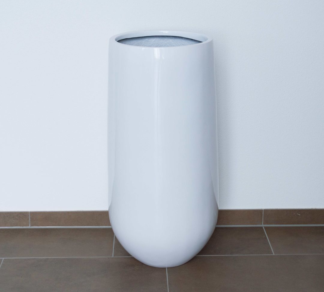 Hochglanz weißer Pflanzkübel aus Fiberglas, rund konisch mit abgerundetem Boden, vor weißer Wand auf braunem Fliesenboden