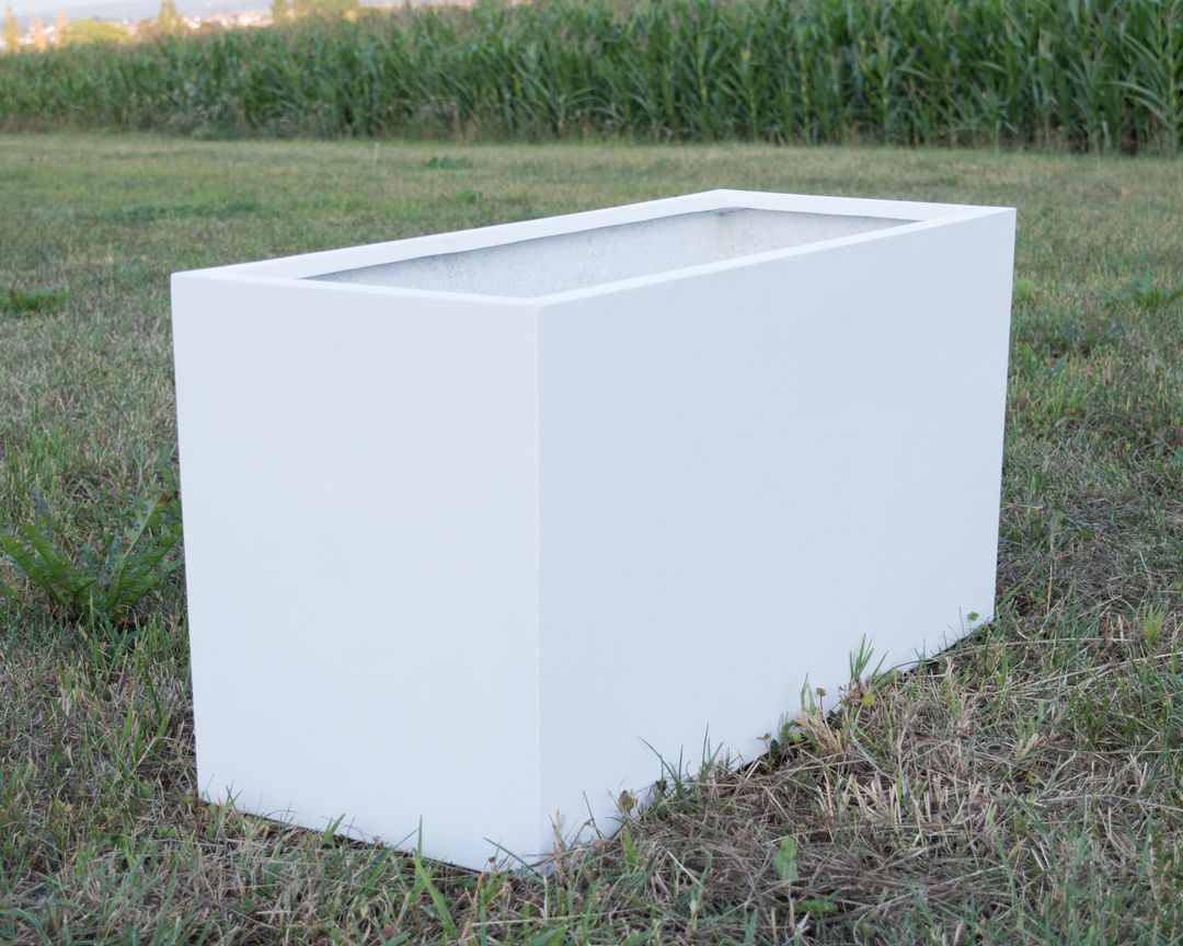 Rechteckiger Pflanzkübel aus Fiberglas in Perlmuttweiß ohne Bepflanzung auf einer Wiese vor einem Maisfeld