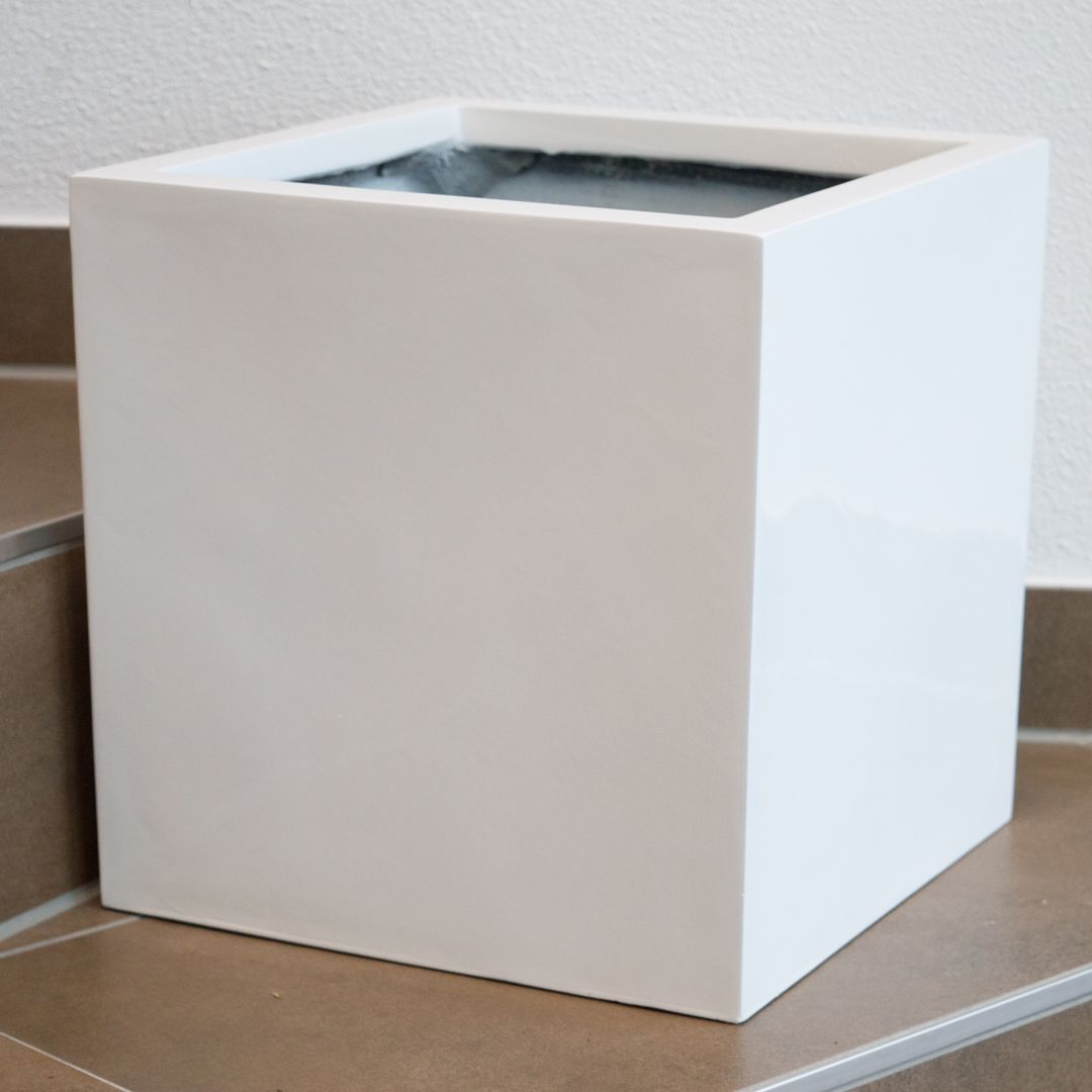 Quadratischer Pflanzkübel aus Fiberglas in Hochglanz Weiß, leer auf braunen Fliesenstufen vor einer weißen Wand