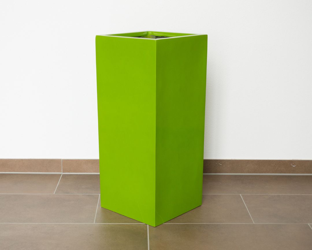 Hochglanz avocadogrüner Pflanzkübel in Säulenform aus Fiberglas, leer auf Fliesenboden vor weißer Wand
