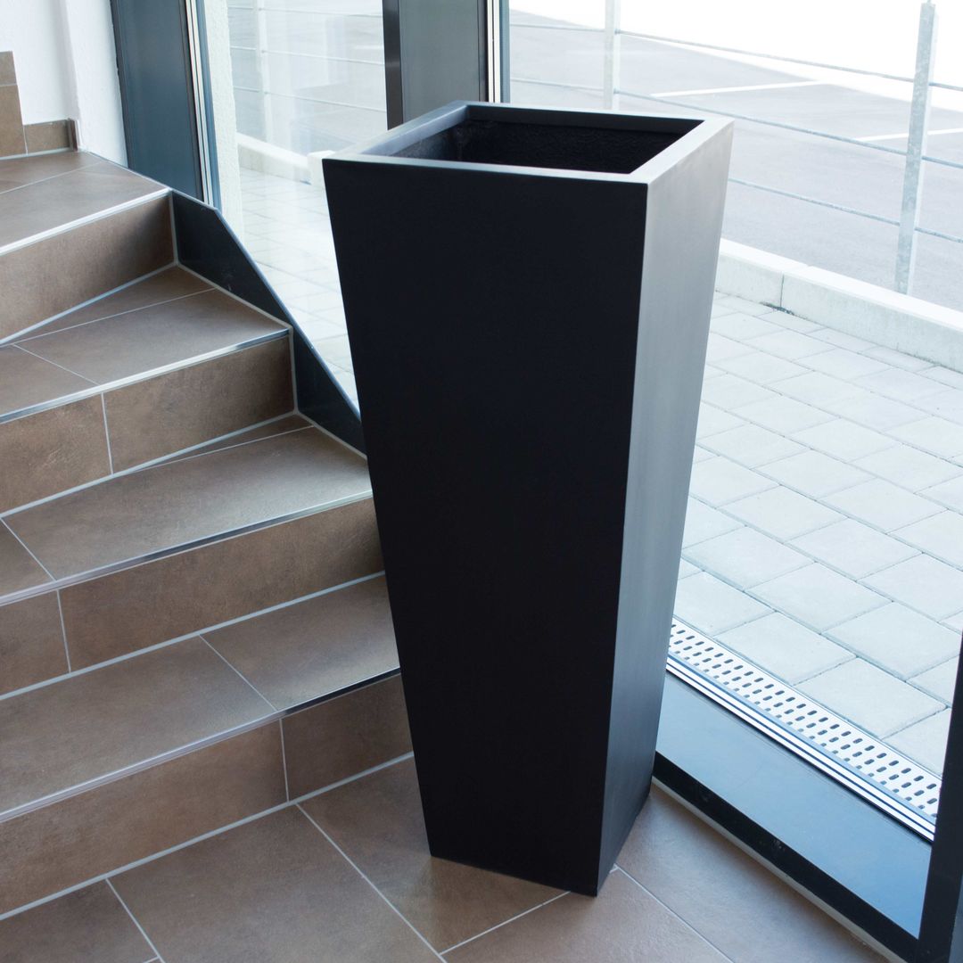 Schwarz-matter Pflanzkübel aus Fiberglas in konischer Säulenform ohne Bepflanzung neben einer Treppe vor einer Glasfront