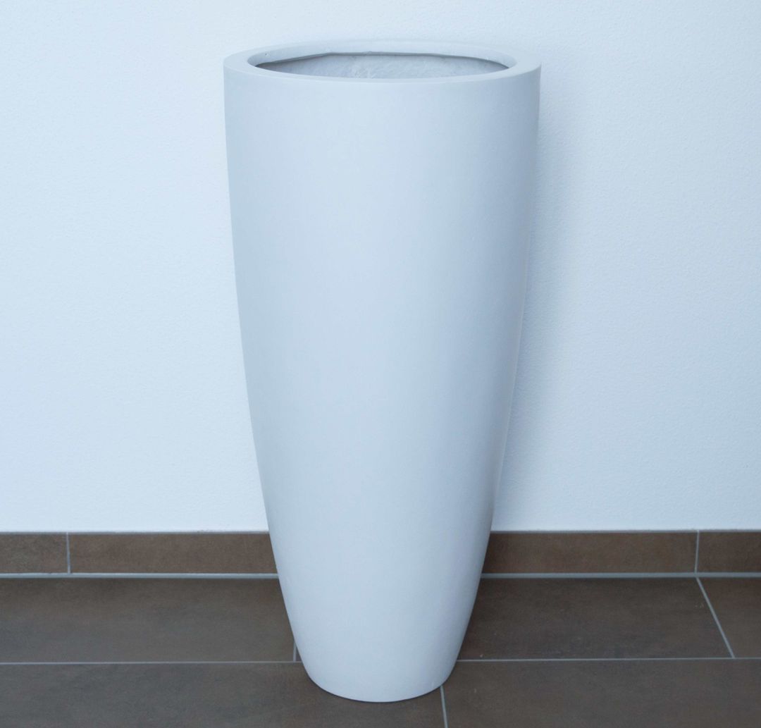 Hoher runder konischer Pflanzkübel aus Fiberglas in Perlmuttweiß, leer vor weißer Wand auf braunem Fliesenboden