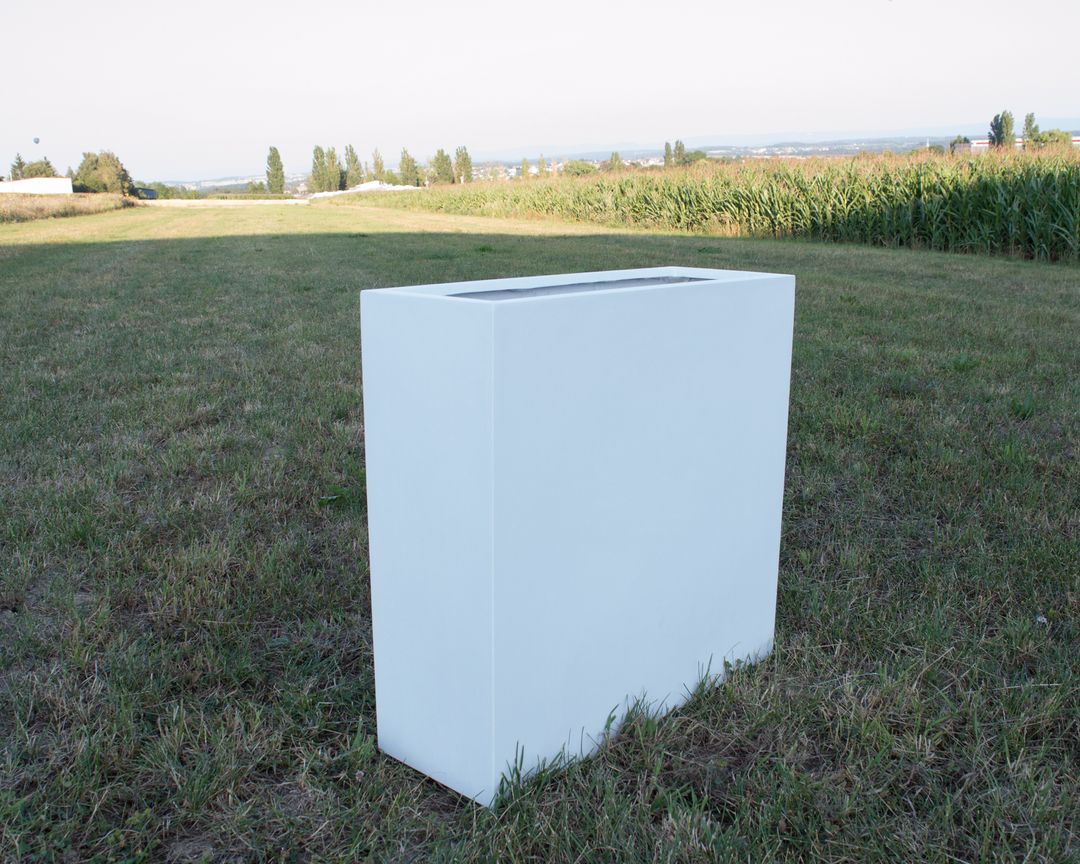 Rechteckiger Pflanzkübel aus Fiberglas in Perlmuttweiß ohne Bepflanzung auf einer Wiese vor einem Maisfeld