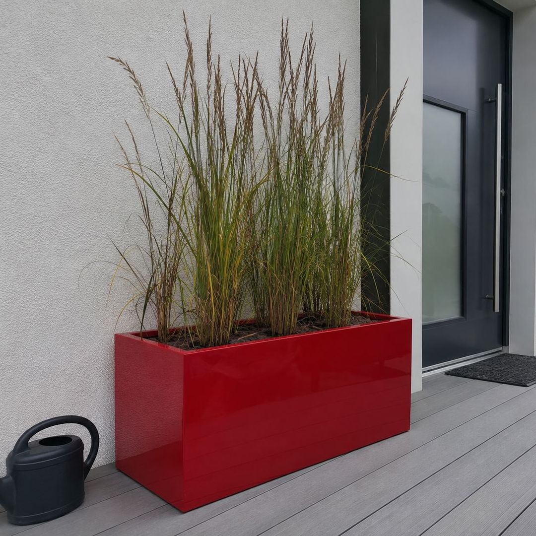 KI-erstellte Abbildung: Rechteckiger Pflanzkübel aus Fiberglas in Hochglanz Rot mit hohen Ziergräsern an der Hauswand neben der Eingangstür