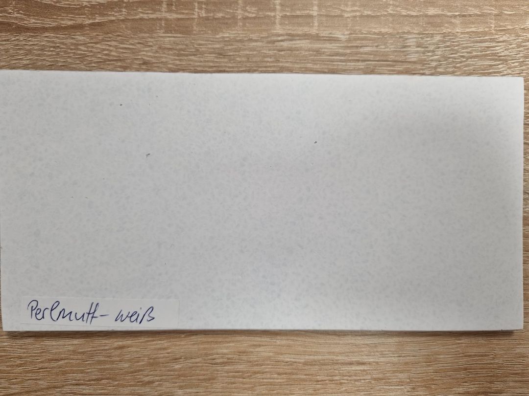 Farbmusterplatte in Perlmuttweiß mit feiner Sprenkelung und handschriftlicher Beschriftung auf einem Holztisch