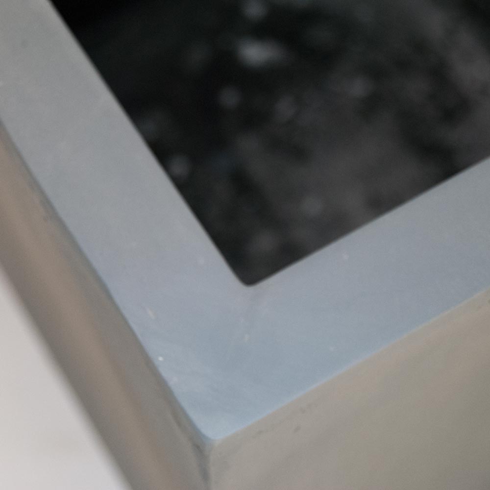 Nahaufnahme der Ecke eines quadratischen Pflanzkübels aus Fiberglas in Grau mit breitem, flachem Rand
