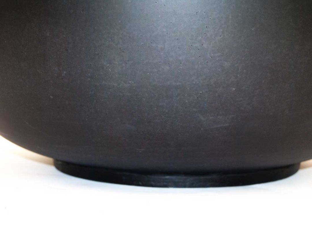 Nahaufnahme des unteren Bereichs einer runden Pflanzschale in Schwarz-Matt mit gewölbter Wand und Standring