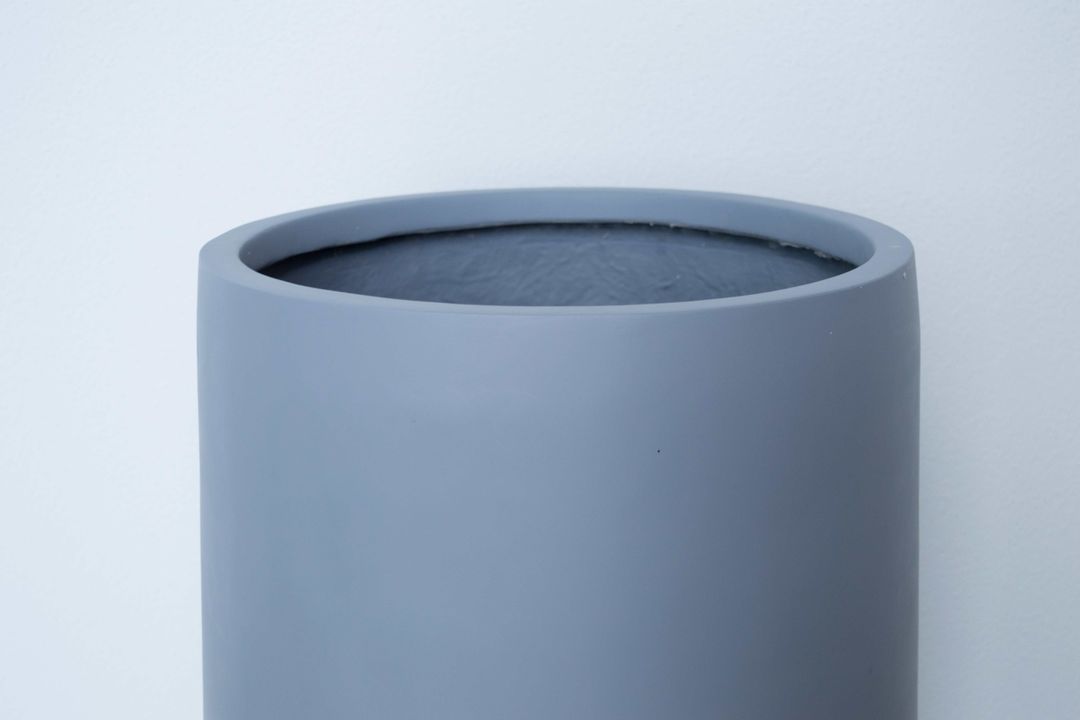 Oberer Rand eines runden grauen Pflanzkübels aus Fiberglas mit Blick ins Innere vor heller Wand