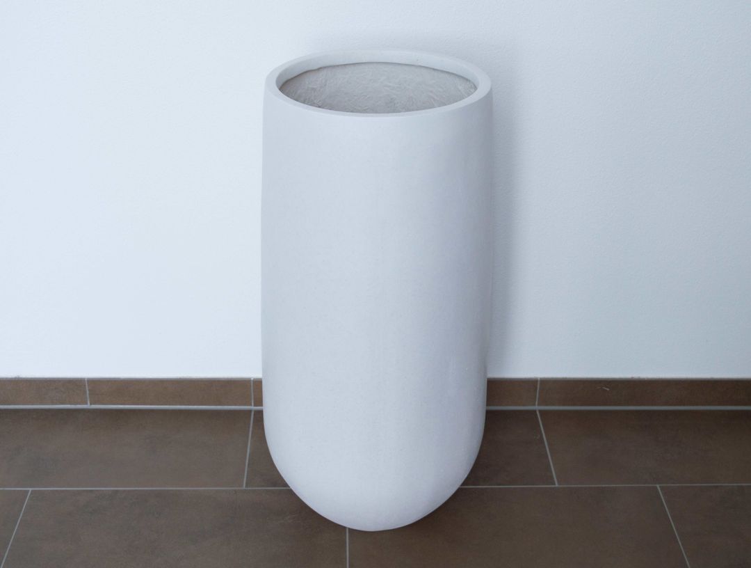 Hoher runder Pflanzkübel aus Fiberglas in Perlmuttweiß ohne Pflanze auf braunem Fliesenboden vor weißer Wand