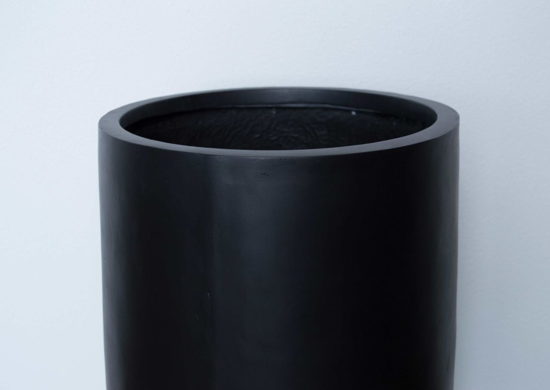 Detailansicht des oberen Rands eines runden, konischen Pflanzkübels aus Fiberglas in Schwarz-matt vor heller Wand