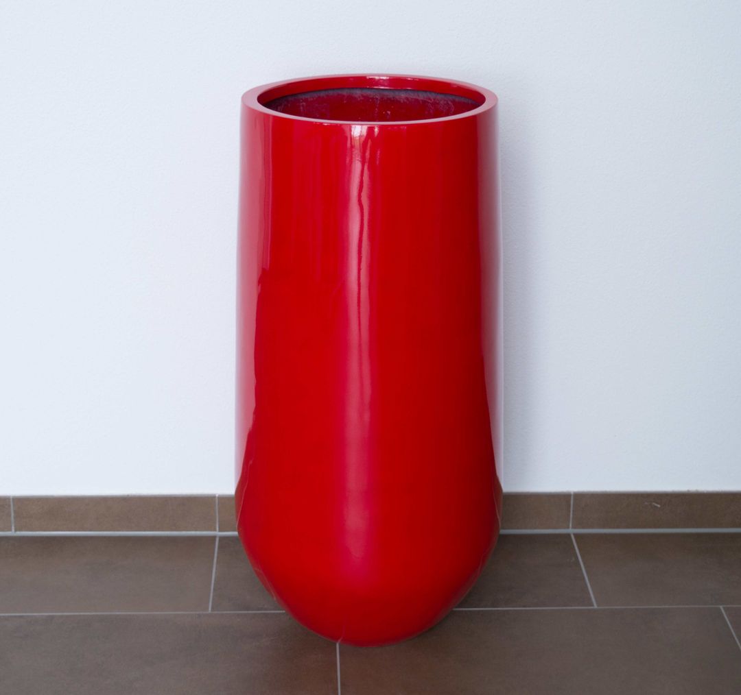 Hoher runder Pflanzkübel aus Fiberglas in Hochglanz Rot, leer vor weißer Wand auf braunem Fliesenboden