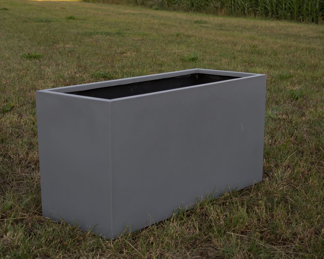 Grauer rechteckiger Pflanzkübel aus Fiberglas ohne Bepflanzung auf einer Rasenfläche vor einem Maisfeld