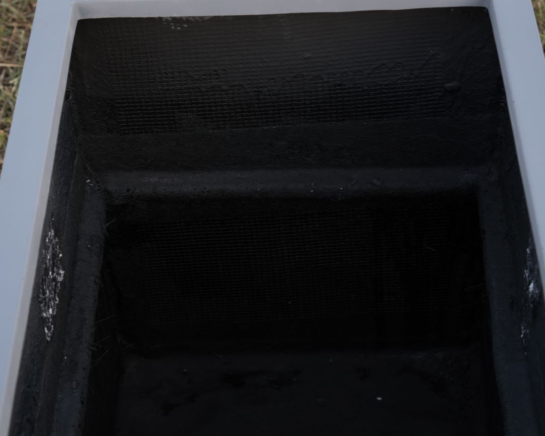 Blick von oben in einen rechteckigen grauen Pflanzkübel aus Fiberglas mit schwarzer Innenseite und innerem Absatz