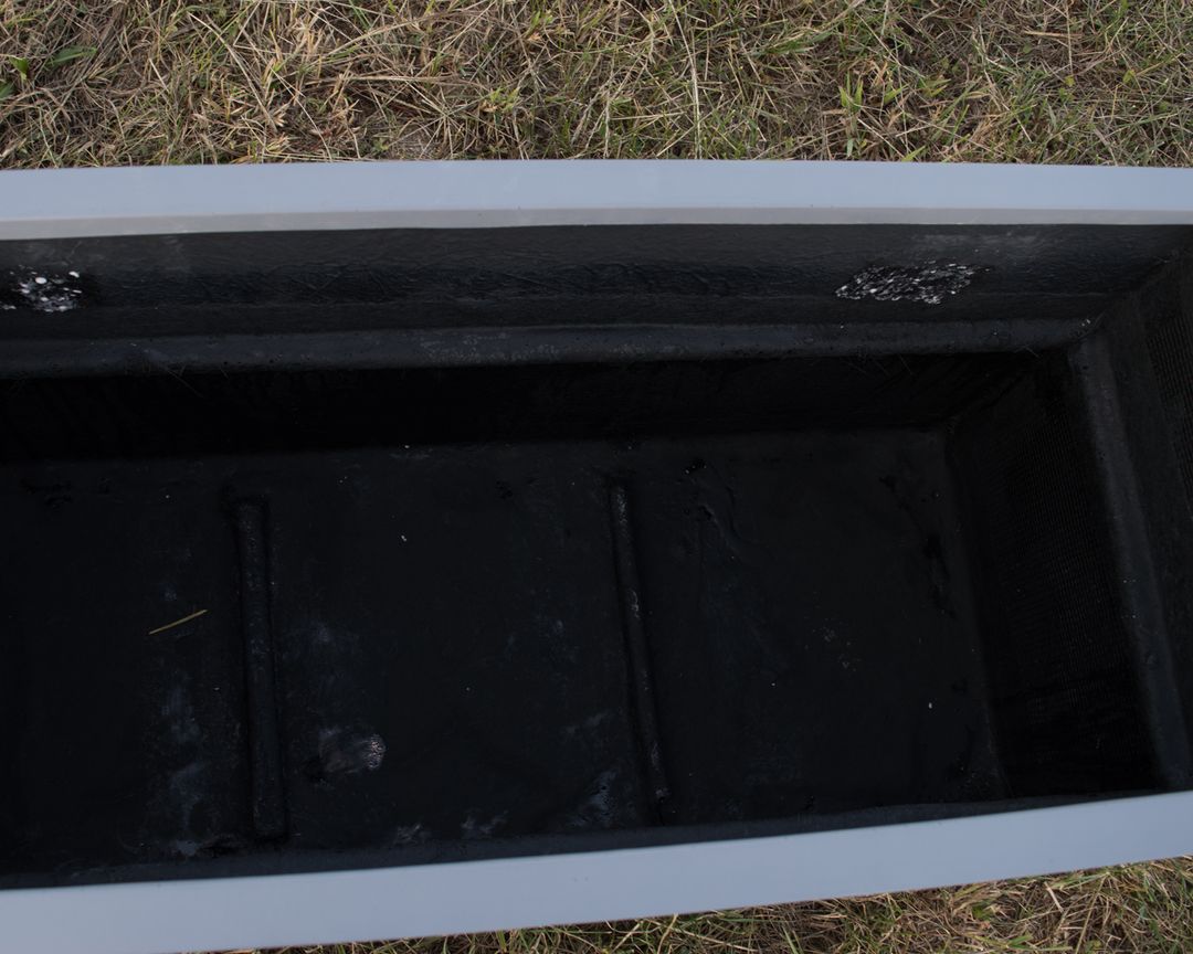 Blick von oben in einen rechteckigen grauen Pflanzkübel aus Fiberglas mit schwarzer Innenseite auf einer Wiese