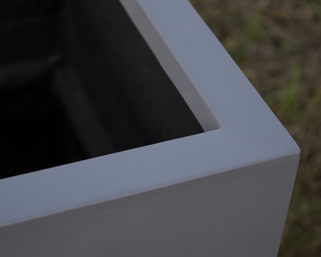 Nahaufnahme der Ecke eines grauen rechteckigen Pflanzkübels aus Fiberglas mit glattem Rand und dunklem Innenraum