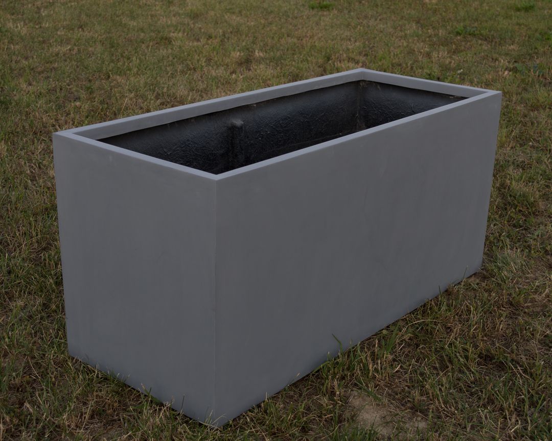 Grauer rechteckiger Pflanzkübel aus Fiberglas ohne Bepflanzung auf einer Rasenfläche, schräg von oben gesehen