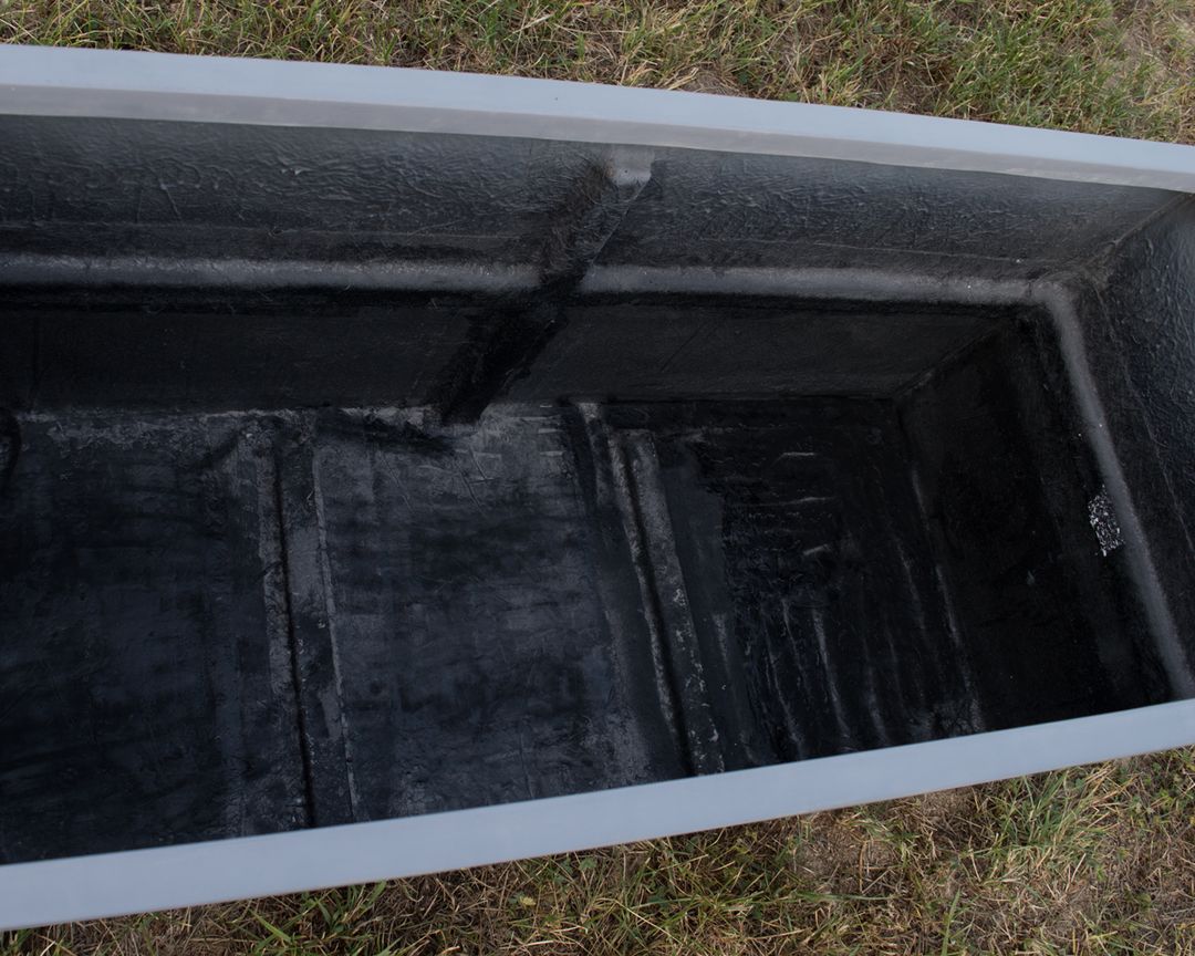 Blick in einen rechteckigen grauen Pflanzkübel aus Fiberglas mit dunkler Innenseite, der auf Rasen steht