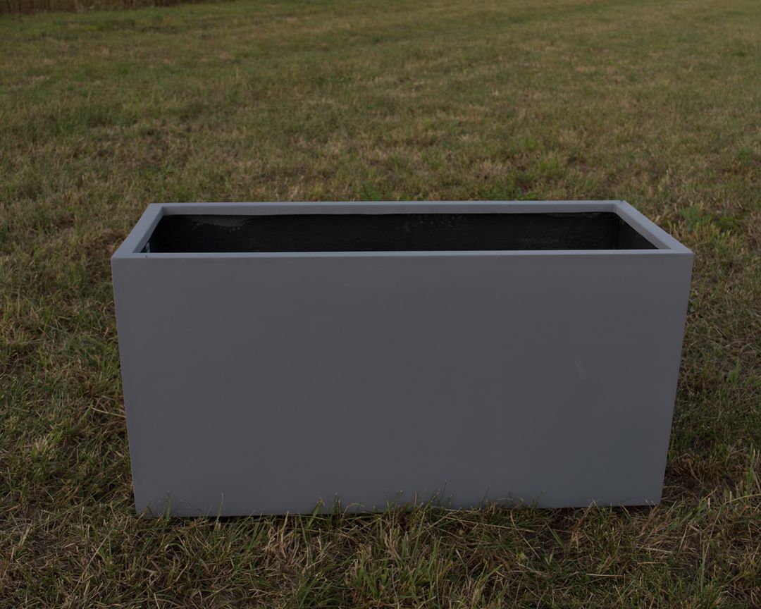 Grauer rechteckiger Pflanzkübel aus Fiberglas ohne Bepflanzung auf einer Rasenfläche im Freien