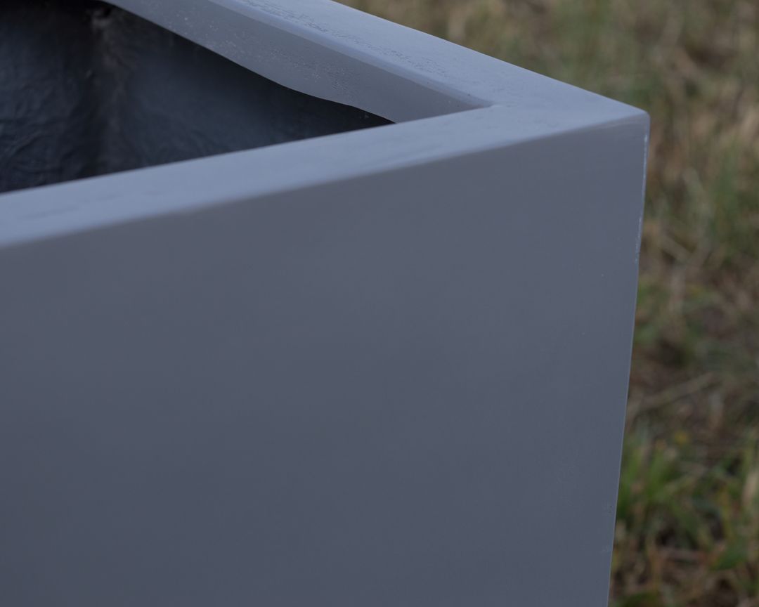Nahaufnahme der Ecke eines grauen rechteckigen Pflanzkübels aus Fiberglas mit glatter Oberfläche vor Rasen
