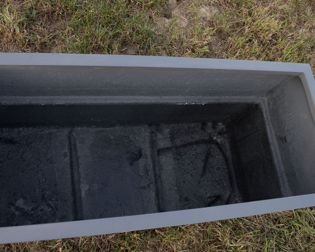 Blick von oben in einen leeren rechteckigen Pflanzkübel in Anthrazit metallic mit dunkler Innenseite auf einer Wiese