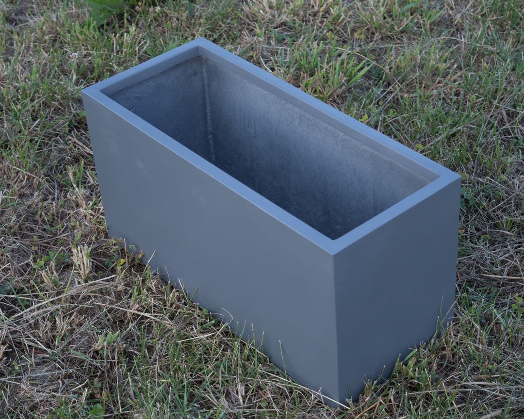 Leerer rechteckiger Pflanzkübel aus Fiberglas in Anthrazit metallic auf einer Rasenfläche, schräg von oben gesehen