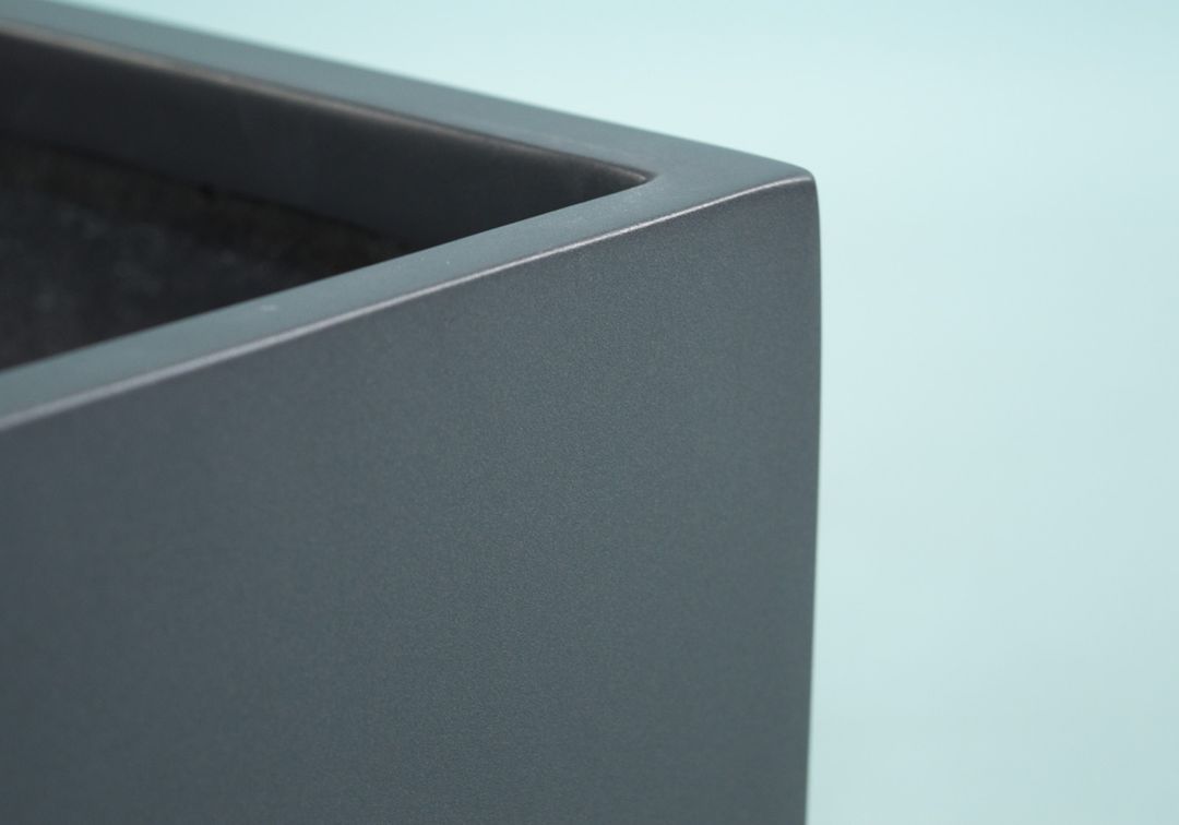 Nahaufnahme der Ecke eines rechteckigen Pflanzkübels aus Fiberglas in Anthrazit-Metallic mit glatter Oberfläche und Rand