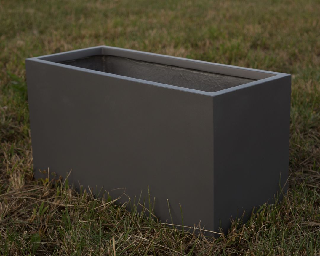 Rechteckiger Pflanzkübel aus Fiberglas in Anthrazit metallic, leer auf einer Wiese mit grünem und trockenem Gras