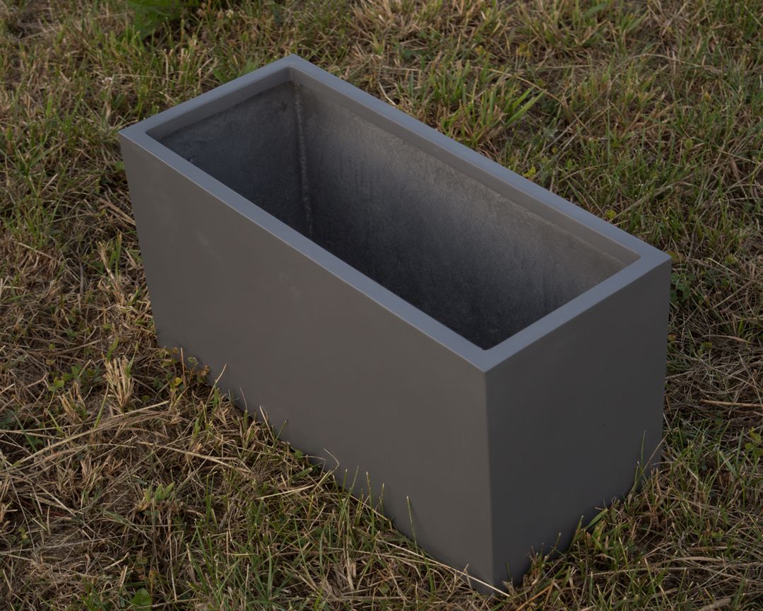 Leerer rechteckiger Pflanzkübel aus Fiberglas in Anthrazit metallic auf einer Rasenfläche, schräg von oben gesehen