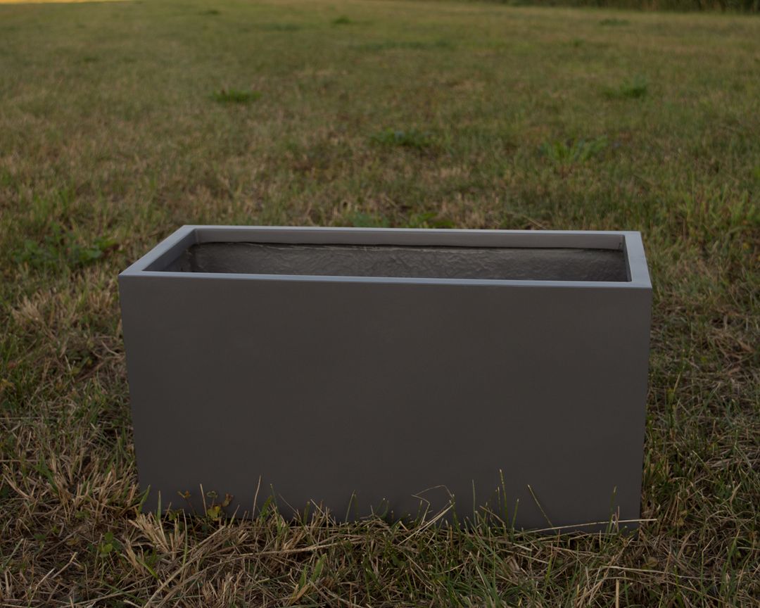 Rechteckiger Pflanzkübel aus Fiberglas in Anthrazit-metallic, leer auf einer Wiese mit trockenem Gras