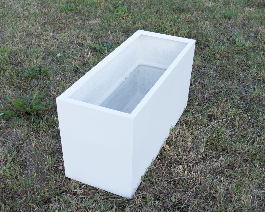 Leerer rechteckiger Pflanzkübel aus Fiberglas in Perlmuttweiß auf einer Rasenfläche, schräg von oben gesehen