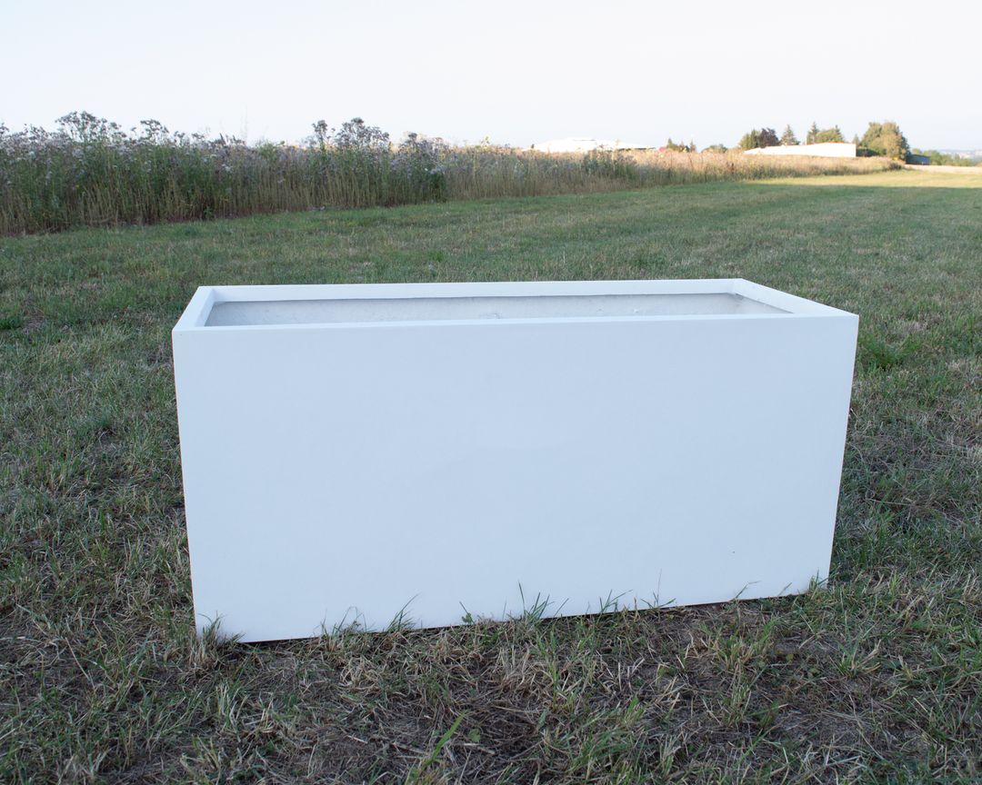Rechteckiger Pflanzkübel aus Fiberglas in Perlmuttweiß ohne Bepflanzung auf einer Wiese vor hohen Gräsern