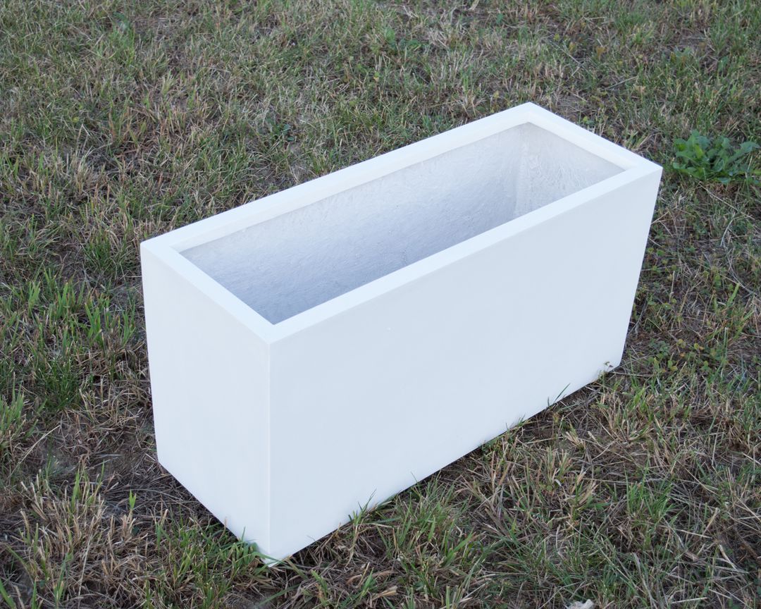 Rechteckiger Pflanzkübel aus Fiberglas in Perlmuttweiß, leer auf einer Rasenfläche im Freien stehend