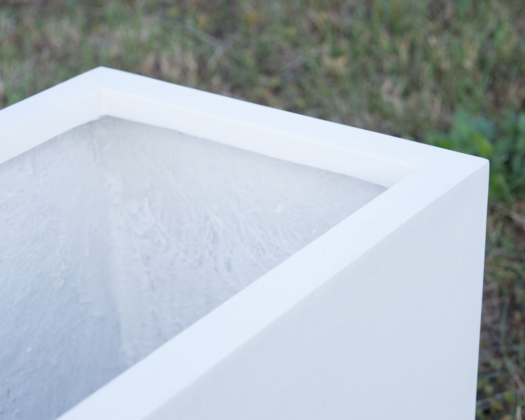 Detailansicht der Ecke eines rechteckigen Pflanzkübels aus Fiberglas in Perlmuttweiß mit Blick ins Innere vor Rasen