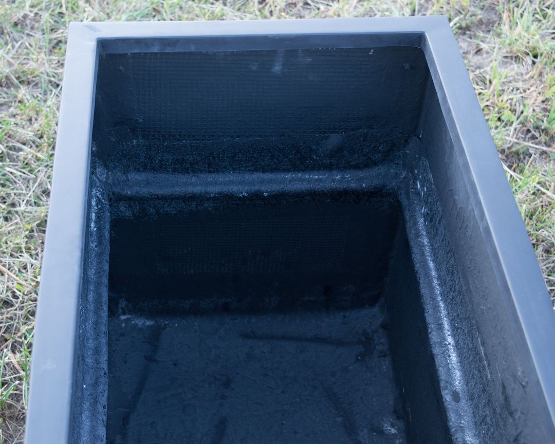 Blick von oben in das Innere eines rechteckigen schwarz-matten Pflanzkübels aus Fiberglas auf Rasen