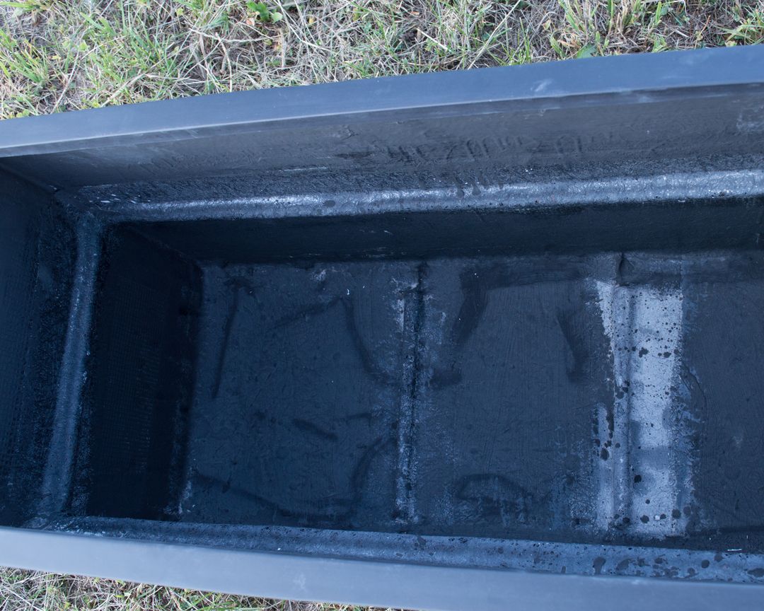 Blick von oben in das Innere eines rechteckigen Pflanzkübels aus Fiberglas in Schwarz-matt auf einer Wiese