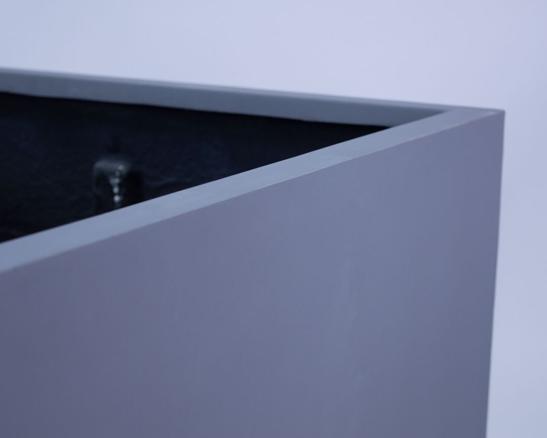 Nahaufnahme der oberen Ecke eines grauen quadratischen Pflanzkübels aus Fiberglas mit glattem Rand und dunklem Innenraum