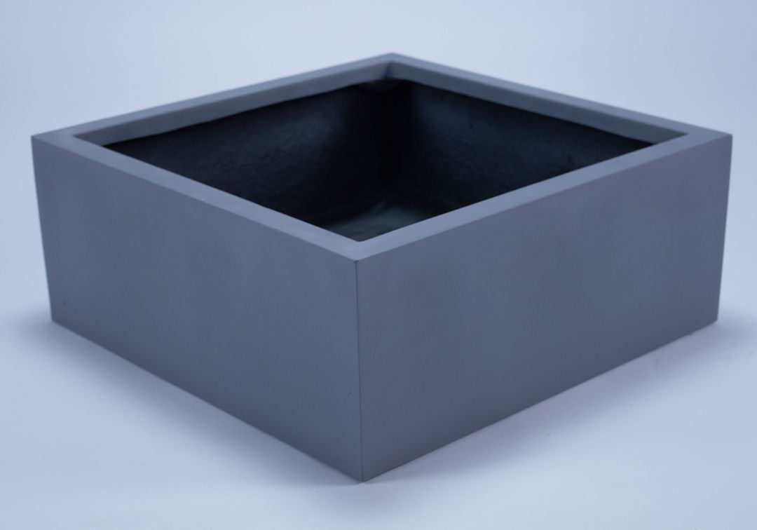 Niedriger quadratischer Pflanzkübel aus Fiberglas in Grau, leer, schräg von oben vor hellem Hintergrund
