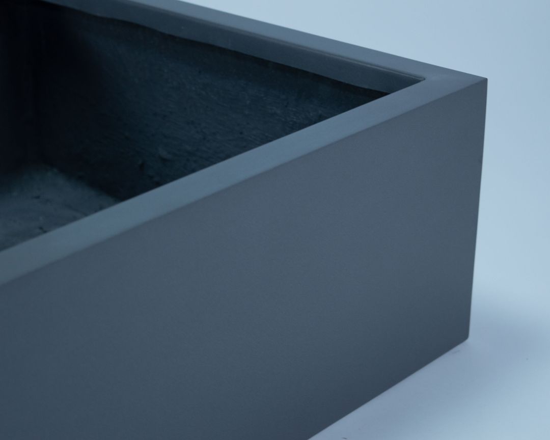 Nahaufnahme der Ecke eines niedrigen quadratischen Pflanzkübels in Anthrazit-Metallic mit glatter Oberfläche und Blick ins Innere