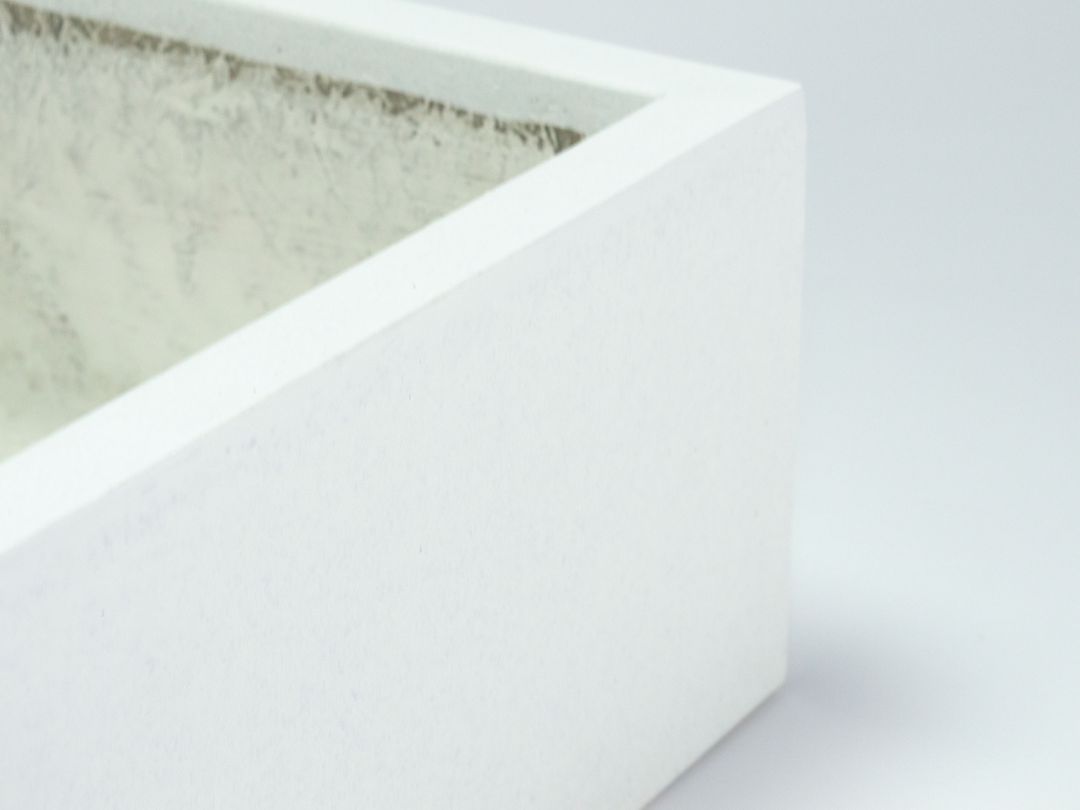 Nahaufnahme der Ecke eines quadratischen Pflanzkübels aus Fiberglas in Perlmuttweiß mit Blick auf Rand und Innenseite