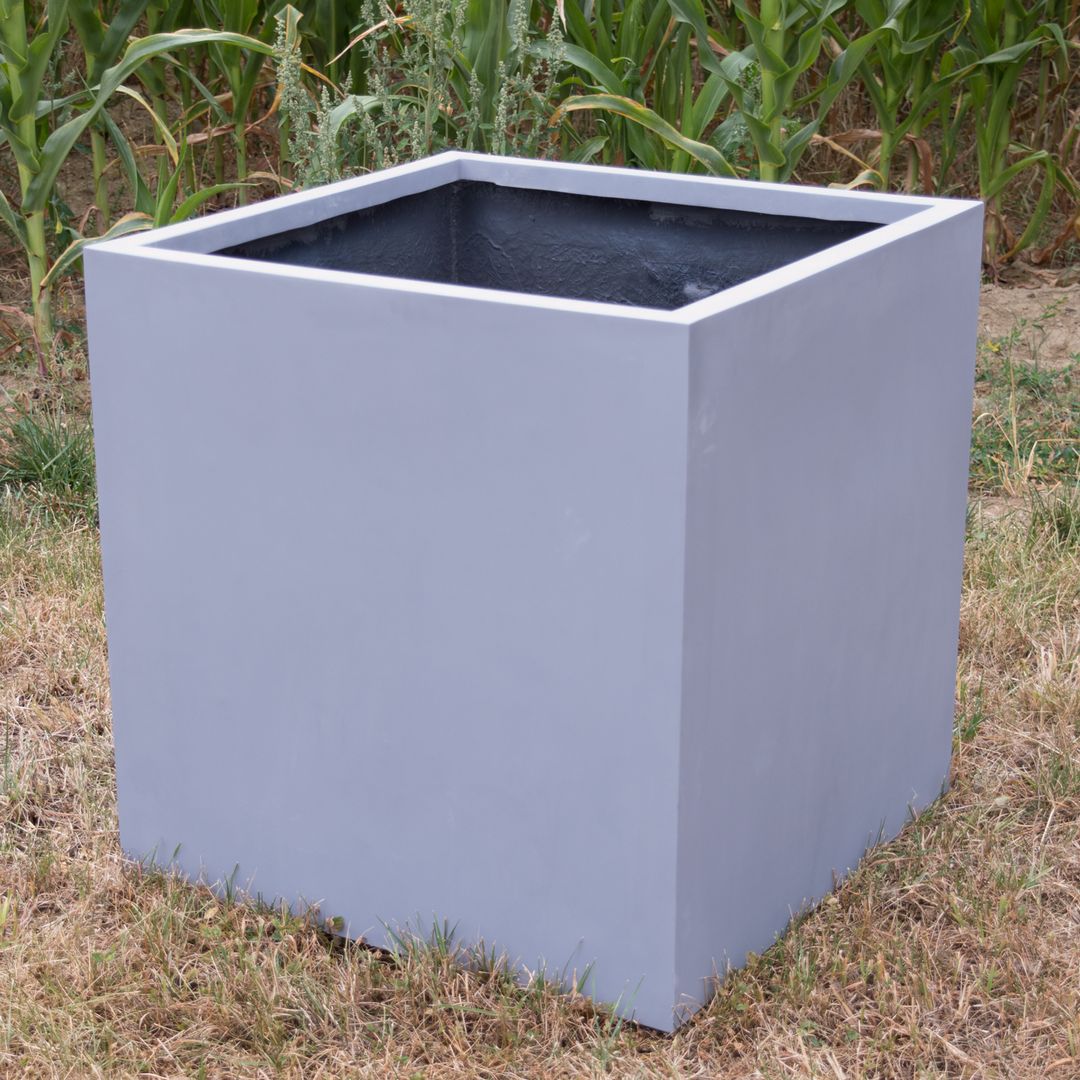 Leerer grauer quadratischer Pflanzkübel aus Fiberglas auf trockener Wiese vor einem Maisfeld