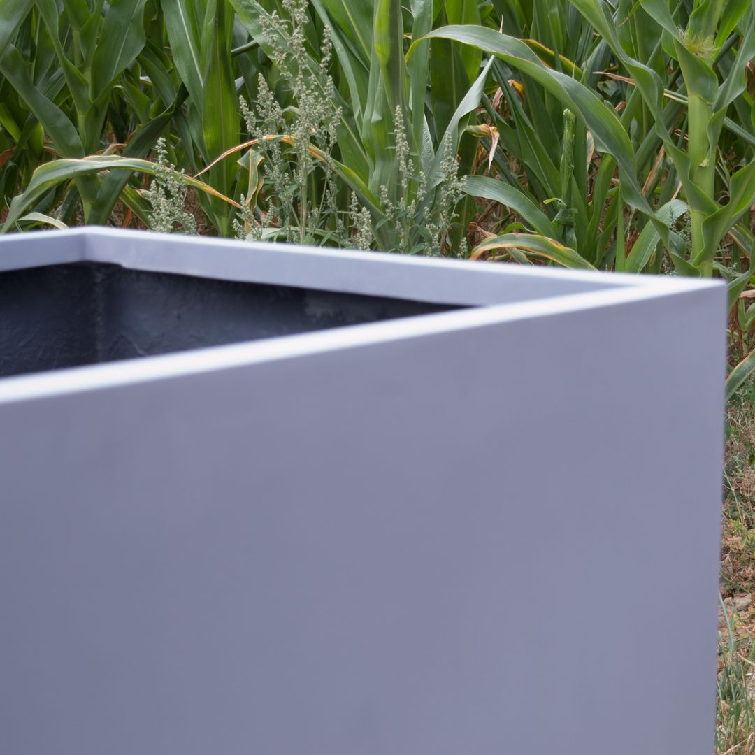Ausschnitt eines grauen quadratischen Pflanzkübels aus Fiberglas mit Blick auf Rand und Ecke vor einem Maisfeld