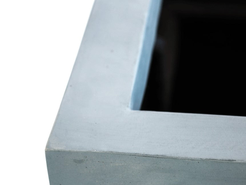 Nahaufnahme der Ecke eines quadratischen grauen Pflanzkübels aus Fiberglas mit breitem, glattem Rand und dunkler Öffnung