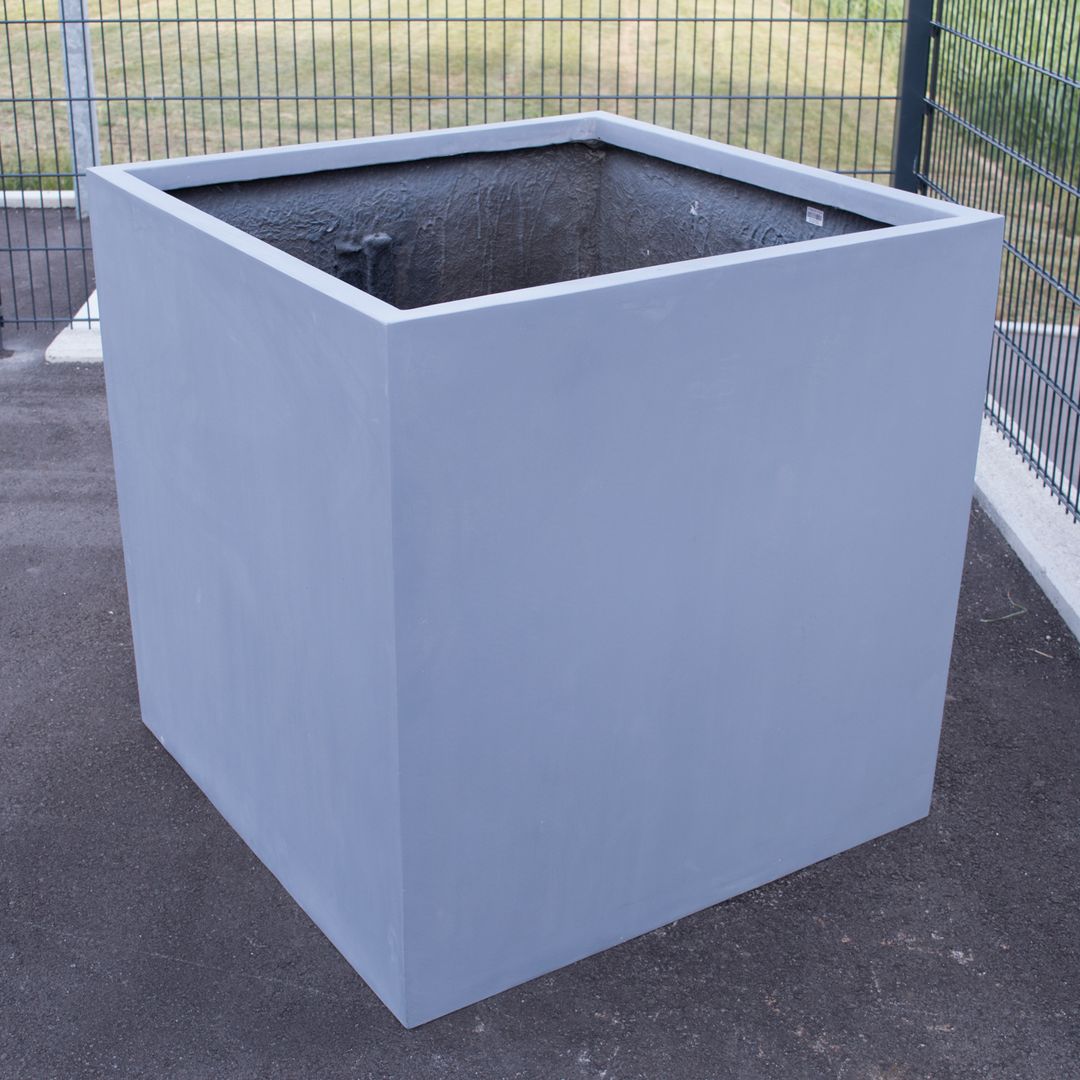 Leerer grauer quadratischer Pflanzkübel aus Fiberglas auf Asphalt vor einem Metallgitterzaun im Freien