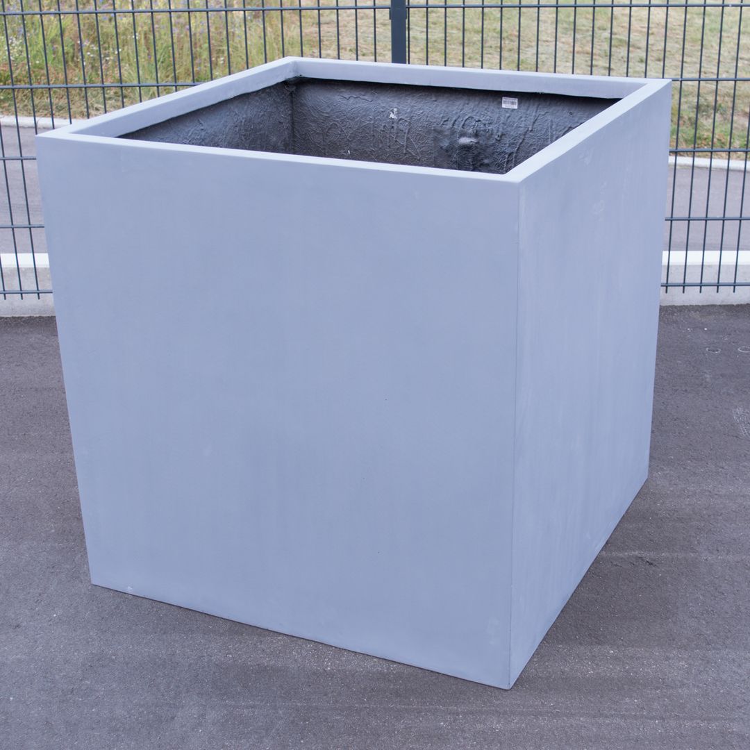 Quadratischer Pflanzkübel aus Fiberglas in Grau, leer auf Asphalt vor einem Metallzaun im Freien