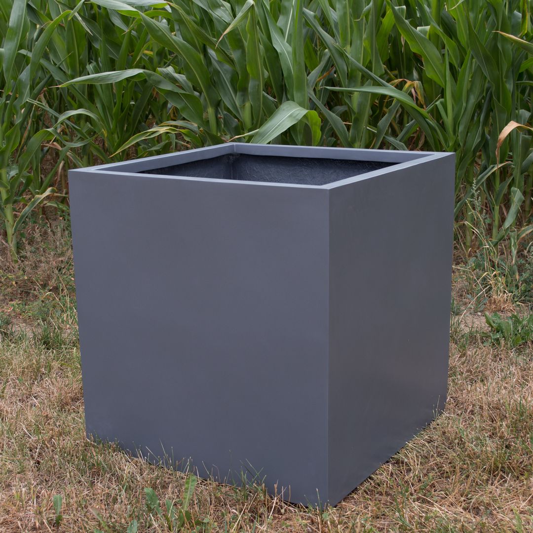 Quadratischer Pflanzkübel aus Fiberglas in Anthrazit metallic, leer auf trockenem Rasen vor einem Maisfeld