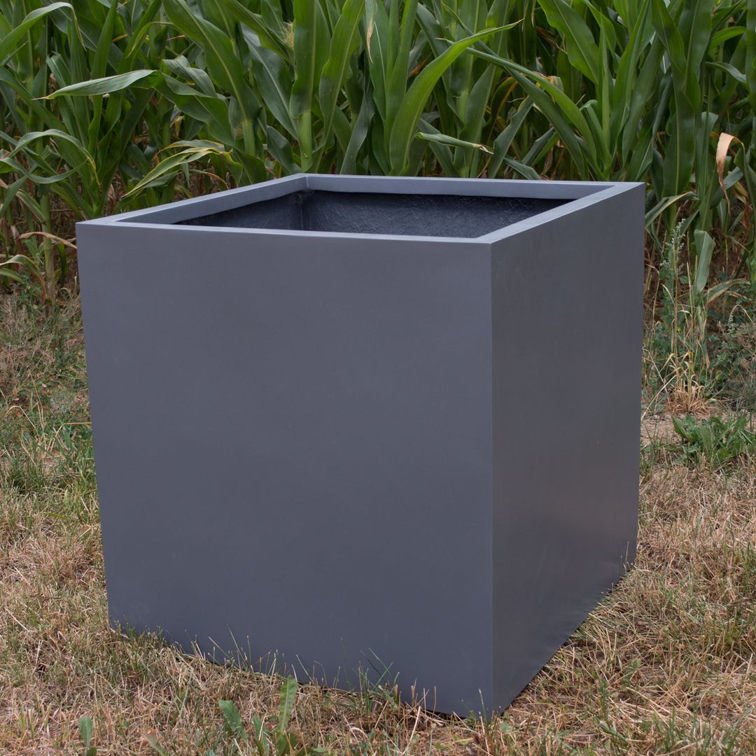 Leerer quadratischer Pflanzkübel aus Fiberglas in Anthrazit metallic auf trockener Wiese vor einem Maisfeld