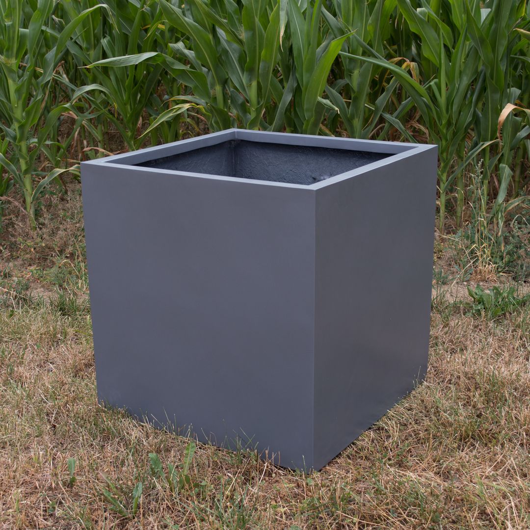 Leerer quadratischer Pflanzkübel aus Fiberglas in Anthrazit metallic auf trockenem Rasen vor einem Maisfeld