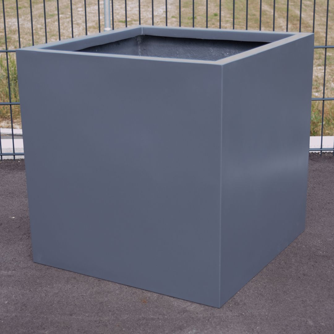 Leerer quadratischer Pflanzkübel aus Fiberglas in Anthrazit metallic auf Asphalt vor einem Metallgitterzaun