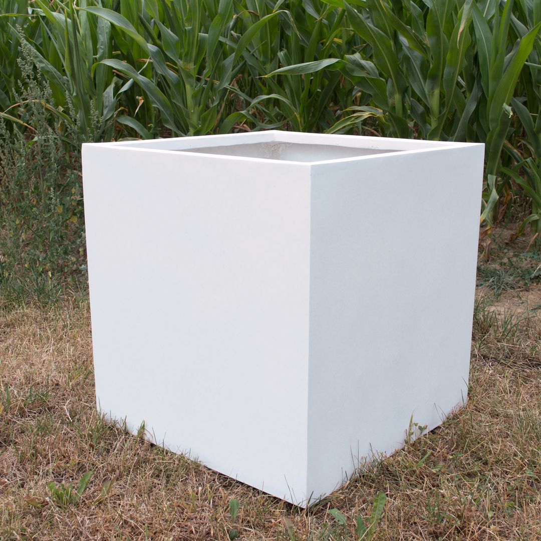 Leerer quadratischer Pflanzkübel aus Fiberglas in Perlmuttweiß auf trockener Wiese vor einem Maisfeld